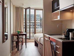 A modern hotel room with a bed, a dining area, a kitchenette, and a balcony with a city view. - Numa The Hague Scheveningen (The Hague)