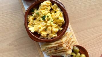 A wooden serving board with scrambled eggs, bread, olives, and condiments.