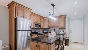 Eine moderne Küche mit Holzschränken, Edelstahlgeräten, einer Arbeitsplatte aus Granit und einer Pendelleuchte.