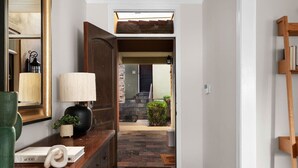 A hallway with a wooden desk, a lamp, and a mirror. There is a door leading to a stone staircase and a door to a room with a green door. - The Lamar Lookout + 3BR + Skyline Views in Austin (Austin)