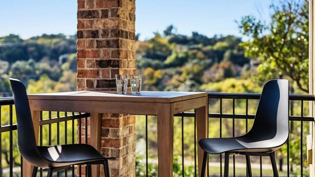 A table with two chairs and two glasses on a balcony with a brick pillar, overlooking a hilly landscape. - The Lamar Lookout + 3BR + Skyline Views in Austin (Austin)