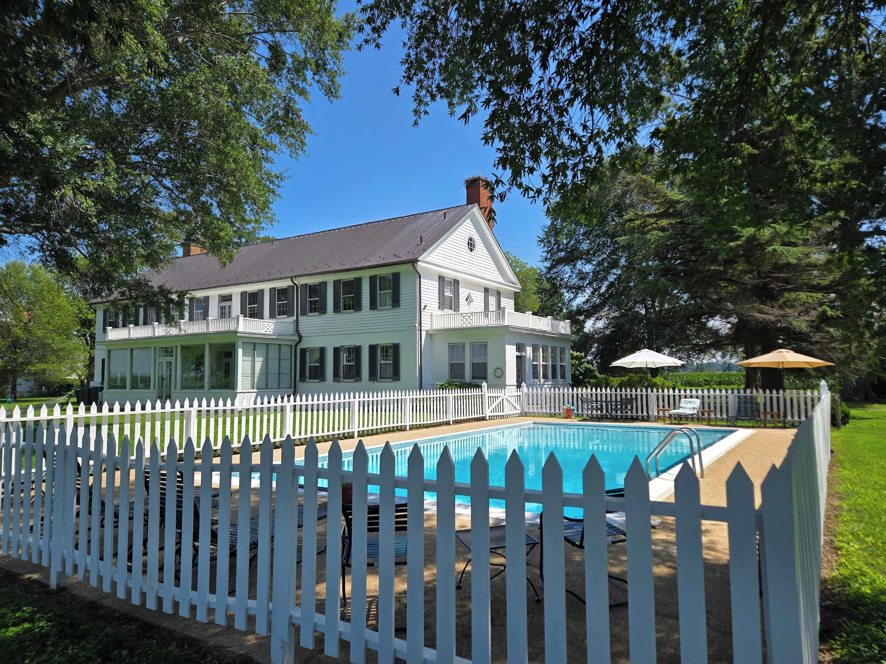 A two-story house with a swimming pool surrounded by a white picket fence.