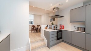 A modern kitchen with grey cabinets, a built-in oven, and a dining area with wooden chairs and a table. - Apartment-sleeps4-parking-100walkingscore (London)