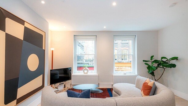 A modern living room with a sectional sofa, a flat-screen TV, two windows with city views, and a large abstract painting. - Apartment-sleeps4-parking-100walkingscore (London)