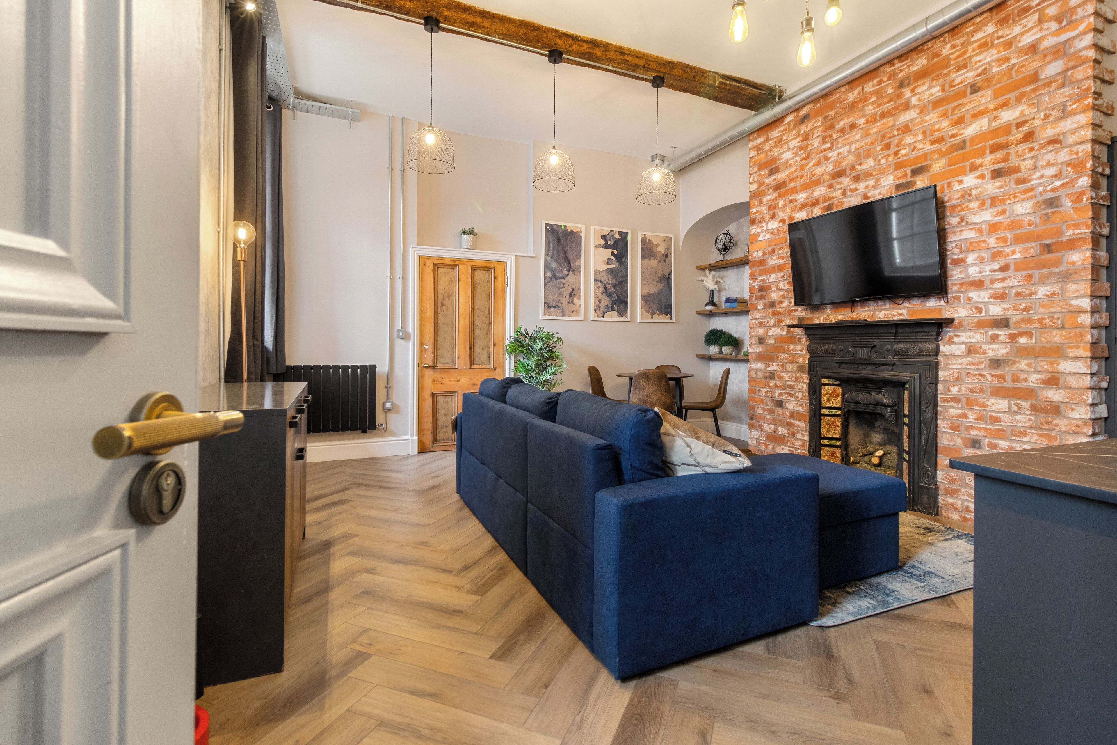 A living room with a brick fireplace, a blue sofa, and a television mounted above it.