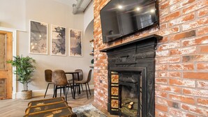 Una sala de estar acogedora con chimenea de ladrillo, un televisor de pantalla plana montado arriba y un comedor con sillas y una mesa.