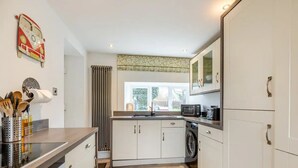 Une cuisine compacte avec des meubles blancs, un four à micro-ondes, un lave-linge et une fenêtre avec des rideaux.