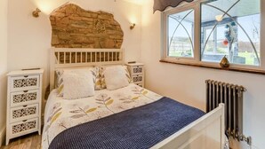 Une chambre avec un mur d’accent en pierre, un lit avec une literie à motifs floraux, un ventilateur de plafond, des tables de chevet et une fenêtre avec vue.