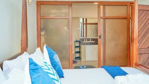 A bedroom with a bed, pillows, a wooden wardrobe, and a bathroom visible through a sliding door. - Sandy Toes, 2br Apt at the beachfront, Diani (Diani Beach)