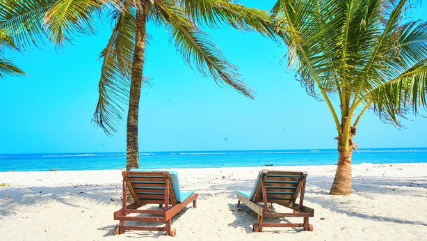 Two wooden lounge chairs on a sandy beach with a clear blue sky and ocean in the background. - Sandy Toes, 2br Apt at the beachfront, Diani (Diani Beach)