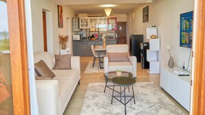 A modern living room with a sofa, armchairs, a coffee table, and a dining area with a table and chairs. - Sandy Toes, 2br Apt at the beachfront, Diani (Diani Beach)