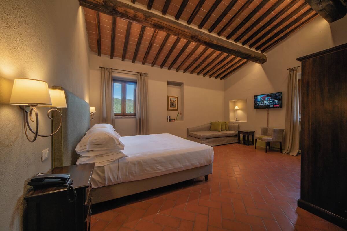 Une chambre d’hôtel comprenant un lit, un bureau avec un téléphone, une télévision et un canapé avec des coussins.
