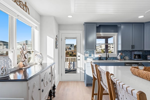 Una cocina moderna con una isla grande, armarios blancos y vistas al exterior.