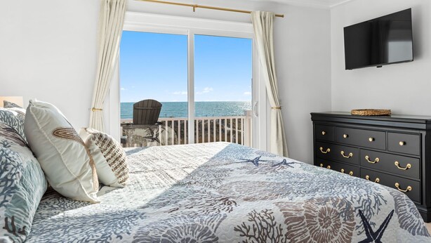 Quarto com cama, cômoda, televisão e varanda vista para o mar.