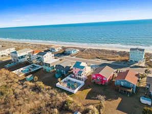 Vista aérea de una zona residencial costera con casas, una piscina y una playa al fondo.