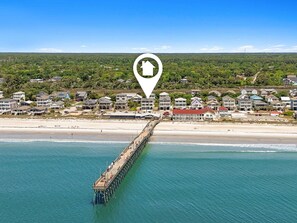 A coastal town with a pier extending into the sea, surrounded by houses and greenery.