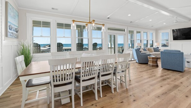 Uma sala de estar ampla com uma mesa de jantar, cadeiras brancas, um sofá azul e vista para o oceano.
