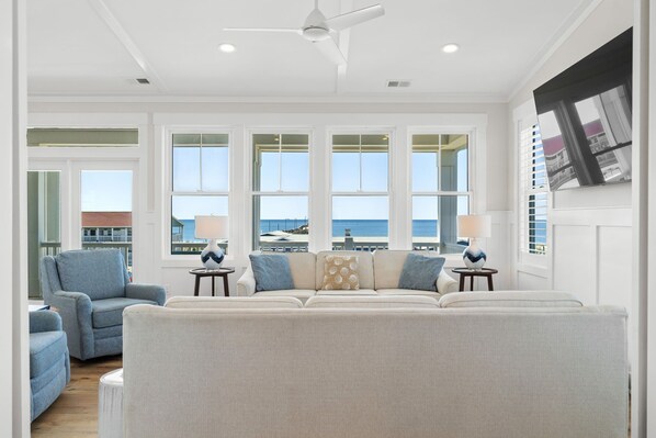 A spacious living room with a large window, a ceiling fan, and a view of the sea.