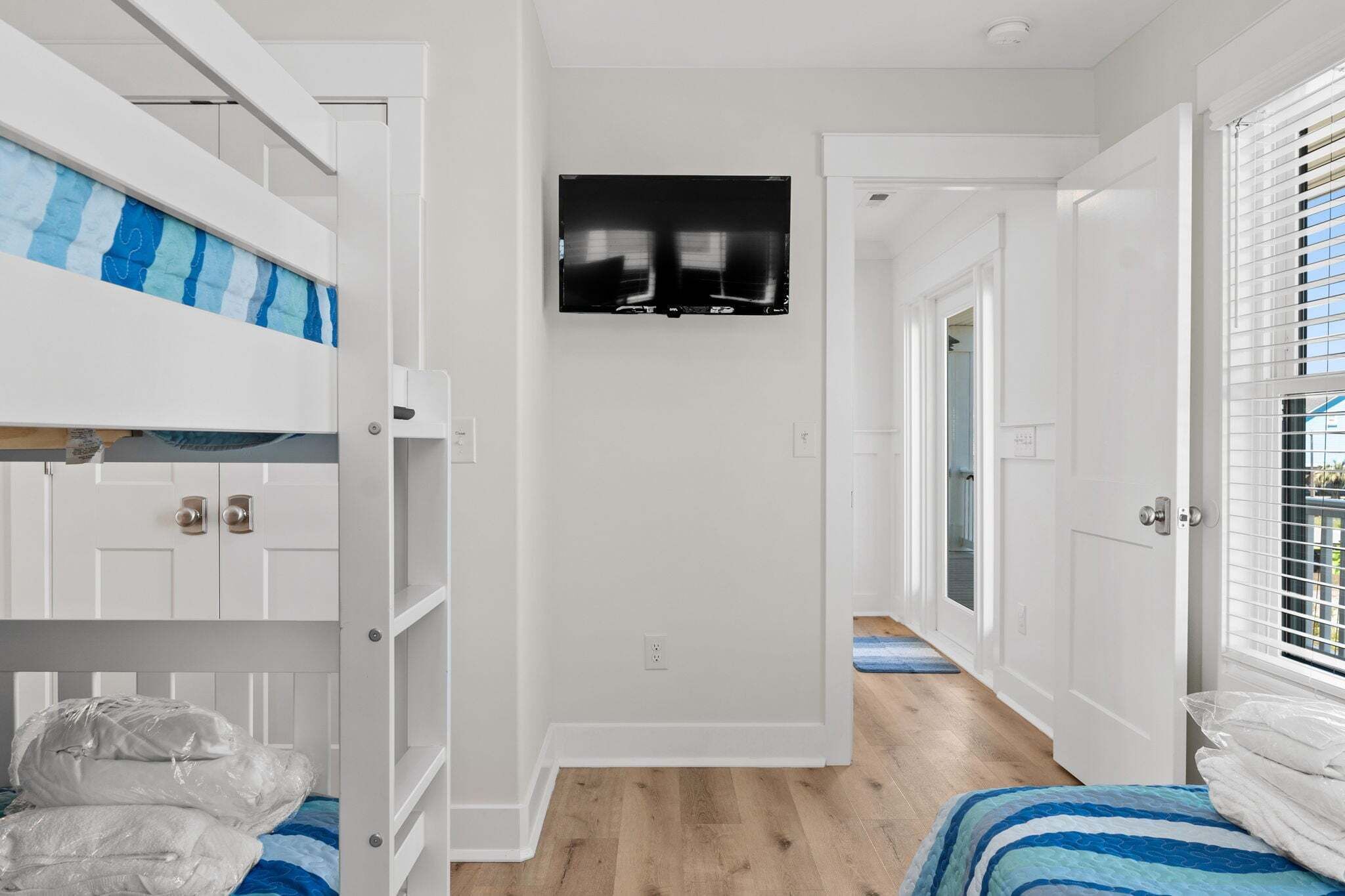 A room with bunk beds, a TV, a wooden floor, and a door leading to another room.