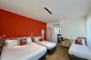 Two single beds with white bedding and red decorative pillows, a wooden desk, and a mirror above it.