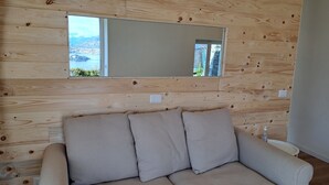 A room with a wooden wall panel design, a beige sofa with cushions, a large mirror, and a view of a lake and buildings. - Apartment with Enchanting View "Shambalahome.it" (STRESA)
