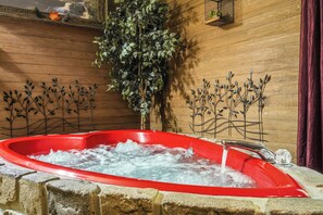 A red hot tub with water running, surrounded by stone walls and decorative metal plants. - FREE Dollywood ticket! cozy cabin for up to 4 w/ hot tub, arcade, deck, Wi-Fi (Sevierville)