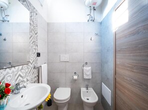 A modern bathroom with a sink, toilet, bidet, and a mirror.