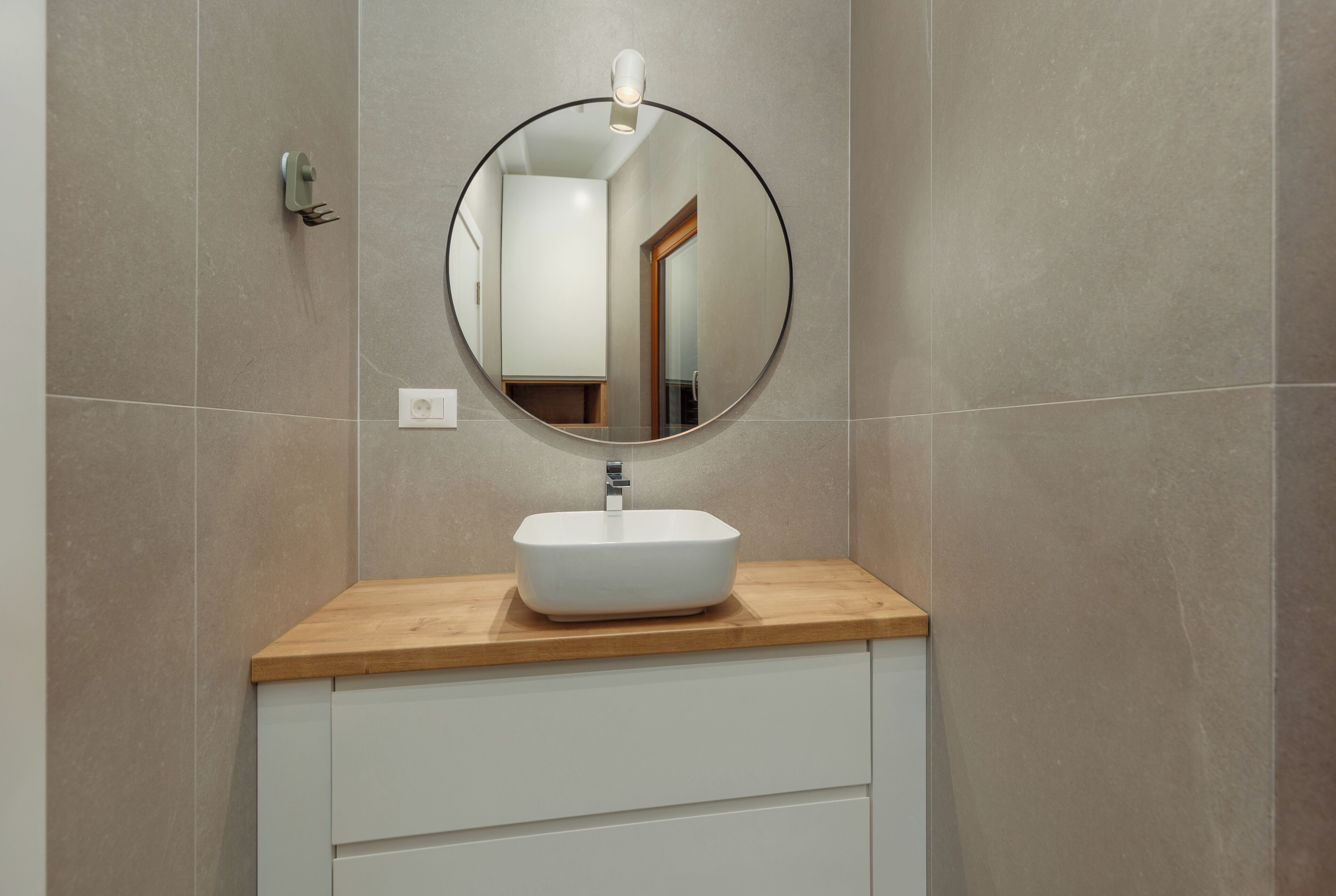A bathroom with a round mirror, a white sink, and a wooden countertop.