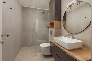 A modern bathroom with a glass-enclosed shower, a white toilet, and a wooden vanity with a large mirror.