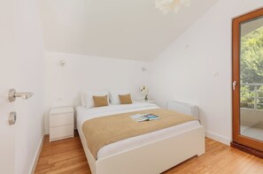 A bedroom with a bed, nightstands, a wooden floor, a window with a view, and a door.