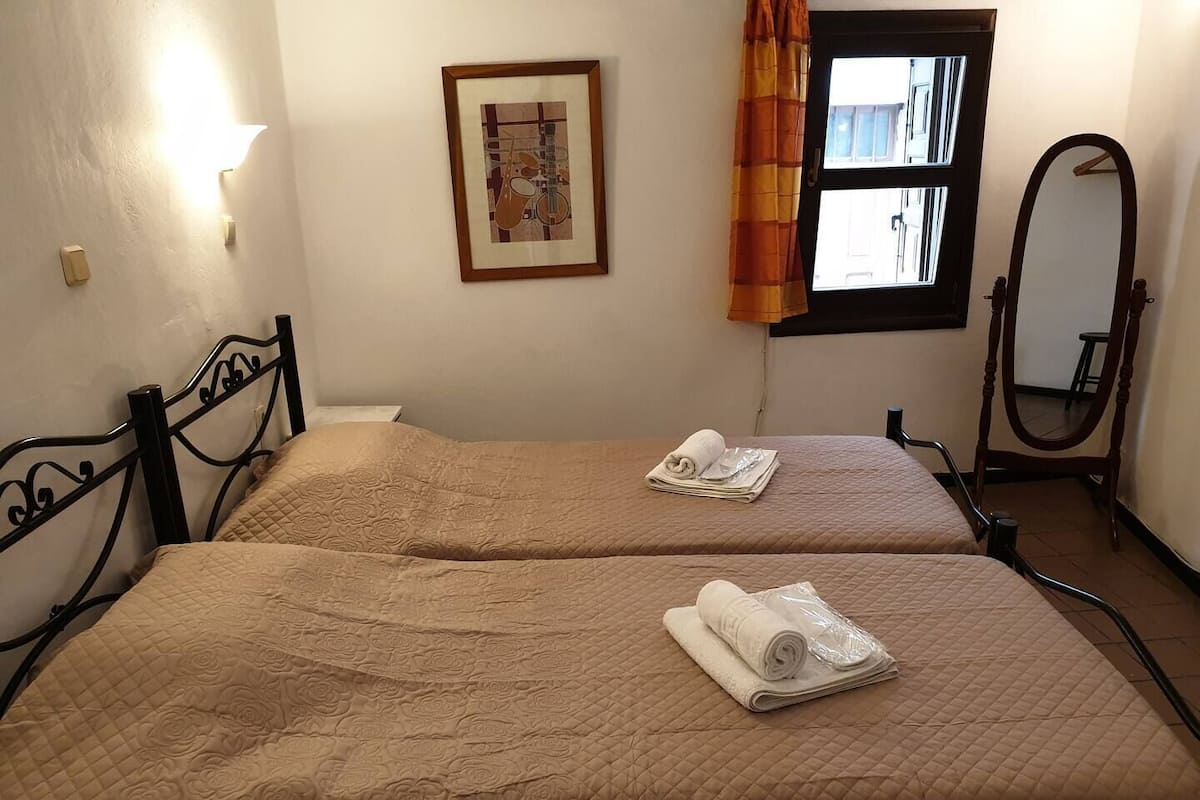 A hotel room with two beds, a framed picture on the wall, a window with curtains, and a mirror.
