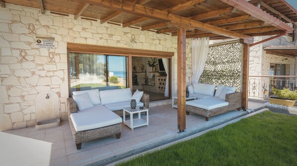 A covered outdoor seating area with wicker furniture and a stone wall backdrop. - Zeus Private Pool Villa, Afitos (Afytos)