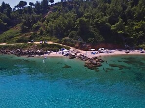 Een kustgebied met helder turquoise water, een rotsachtige kustlijn en een strand met parasols en ligbedden.