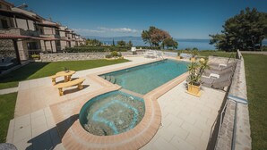 Une piscine avec vue sur la mer, entourée d’une terrasse en pierre, d’un espace détente avec des fauteuils et d’un bâtiment en pierre en arrière-plan.