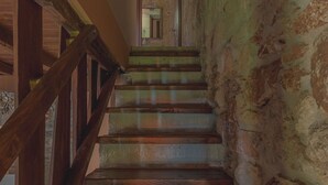 Un escalier en bois, avec des murs en pierre, mène à une pièce dotée d’une porte en bois et d’un miroir.