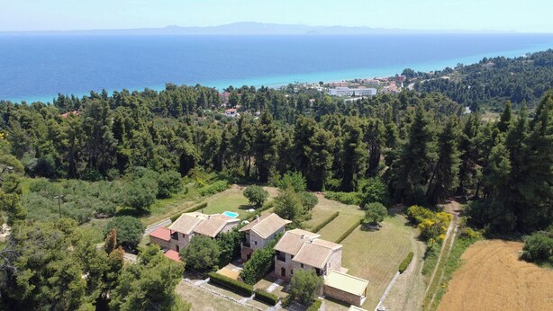 Vue aérienne d’une propriété comprenant deux bâtiments, une vaste zone boisée et une vue sur la mer.