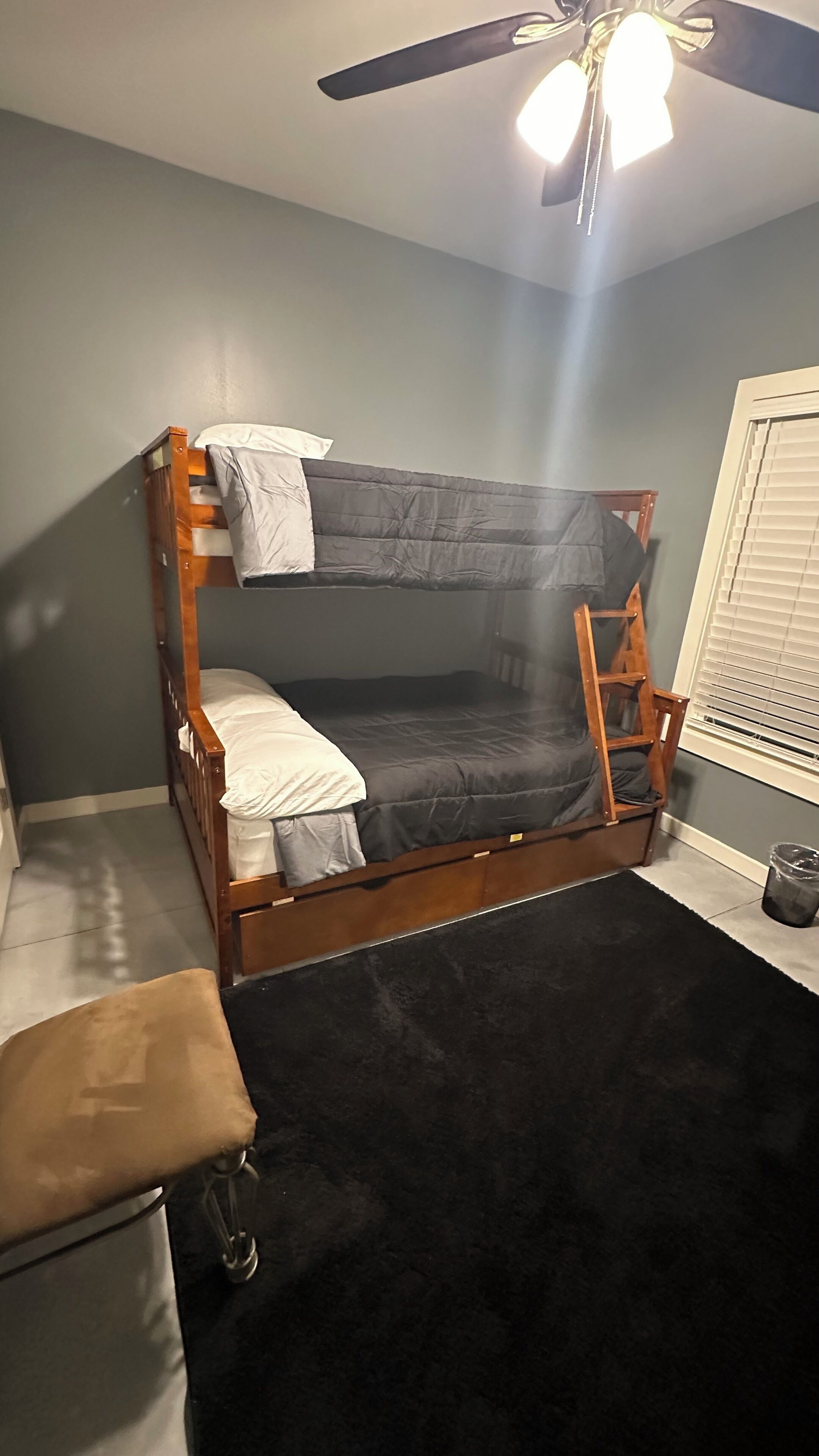 A bunk bed with a ladder, a small chair, and a window with blinds.