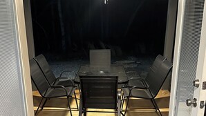 Un patio descubierto con mesa y sillas, un ventilador de techo y vista al jardín trasero.