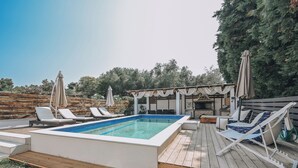 A swimming pool with lounge chairs and umbrellas, surrounded by a wooden deck and a covered barbecue area. - Callisto Private Pool Villa, Pefkochori (Pefkochori)