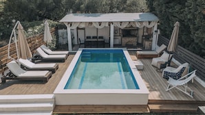 A rectangular pool with a wooden deck, surrounded by lounge chairs and umbrellas. - Callisto Private Pool Villa, Pefkochori (Pefkochori)