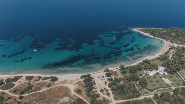 An aerial view of a coastal area with a beach, clear blue waters, and a marina. - Callisto Private Pool Villa, Pefkochori (Pefkochori)