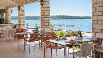An outdoor dining area with stone pillars, wicker chairs, and tables overlooking a body of water.