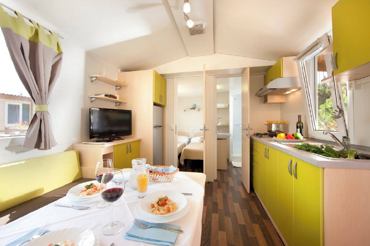 Cocina compacta con comedor, televisor y ventana con cortinas.