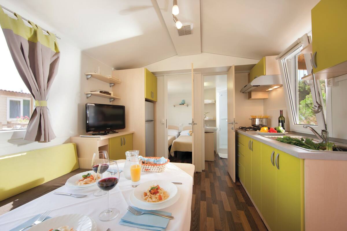 Una cocina compacta con comedor, televisor y ventana con cortinas.