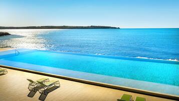 A pool with a view of the sea, surrounded by lounge chairs.