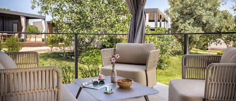 A balcony with wicker furniture, a table with a vase and a bowl, and a view of greenery and buildings.