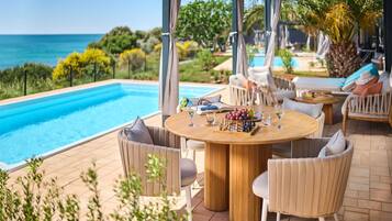 Zona junto a la piscina con vista al mar, una mesa redonda de madera con sillas y un pequeño tablero de ajedrez.