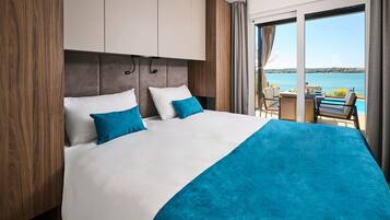 A hotel room with a bed, a view of the water, and a balcony with a table and chairs.