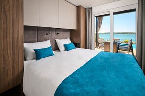 Habitación de hotel con cama, vista al agua y balcón con mesa y sillas.