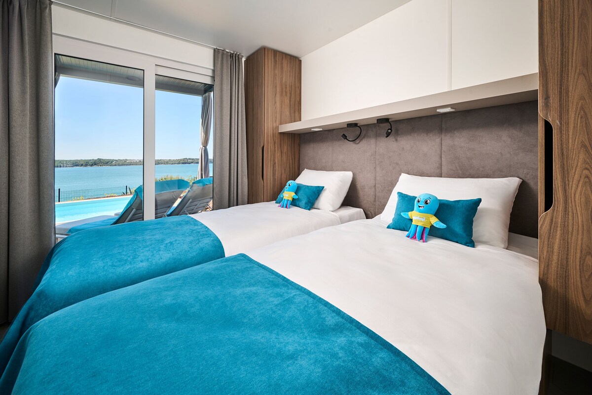 A hotel room with two beds, a large window with a view of a body of water, and a wooden headboard.
